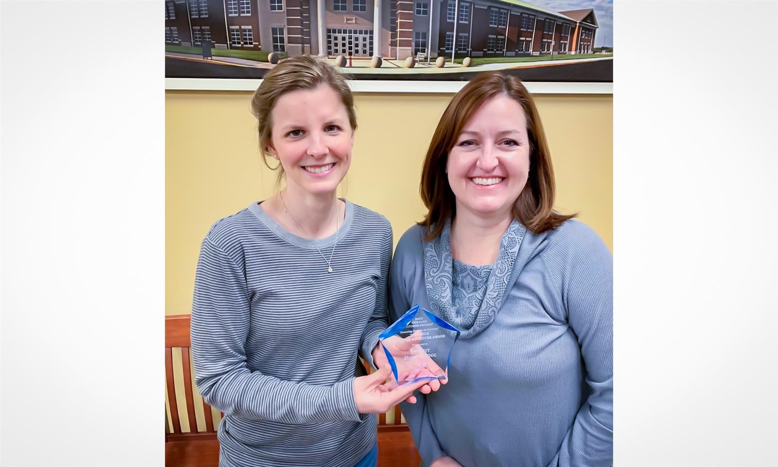 Two teachers hold up a glass trophy 